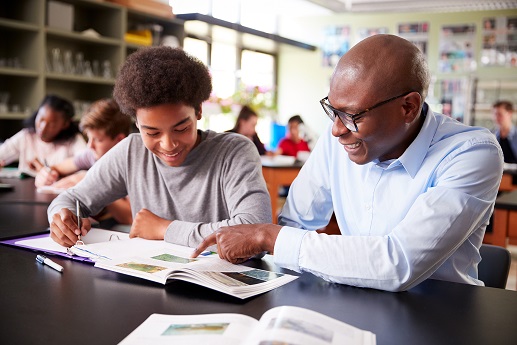 High School Tutor Sitting At Desk With Male Student In Biology Class