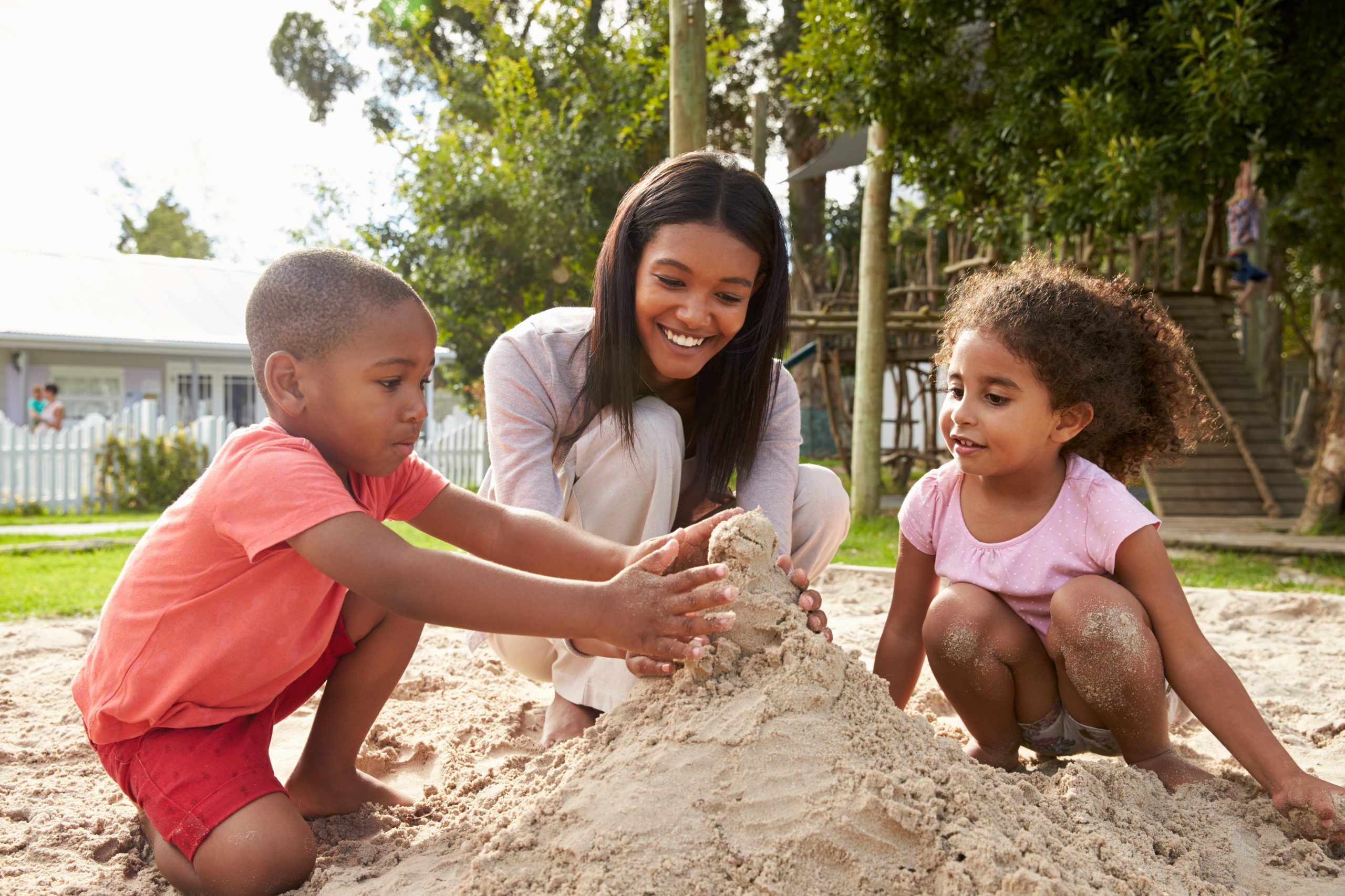 Teacher playing with two children in the sand.