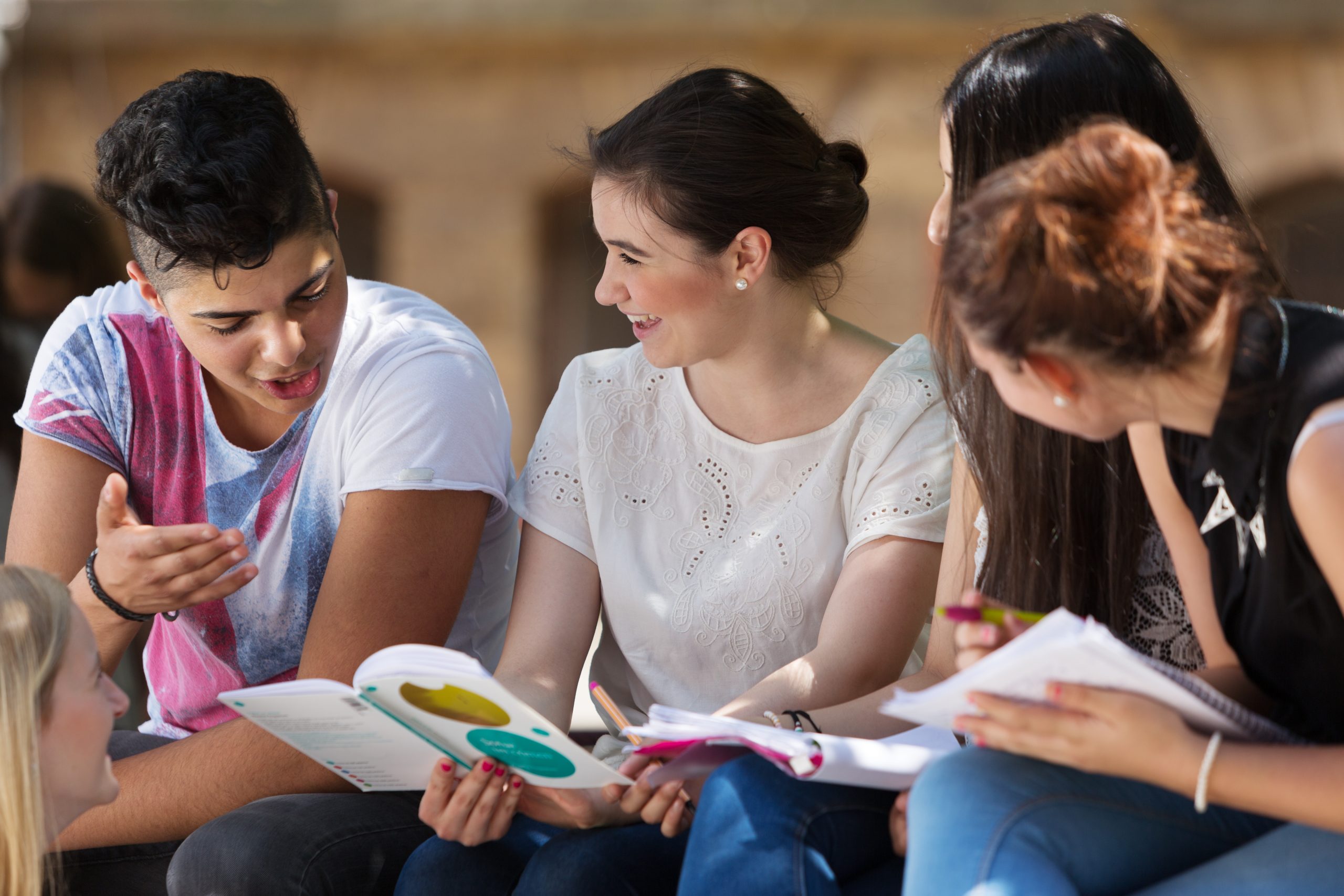 Group of students Group of students sitting outside looking at a book and talking