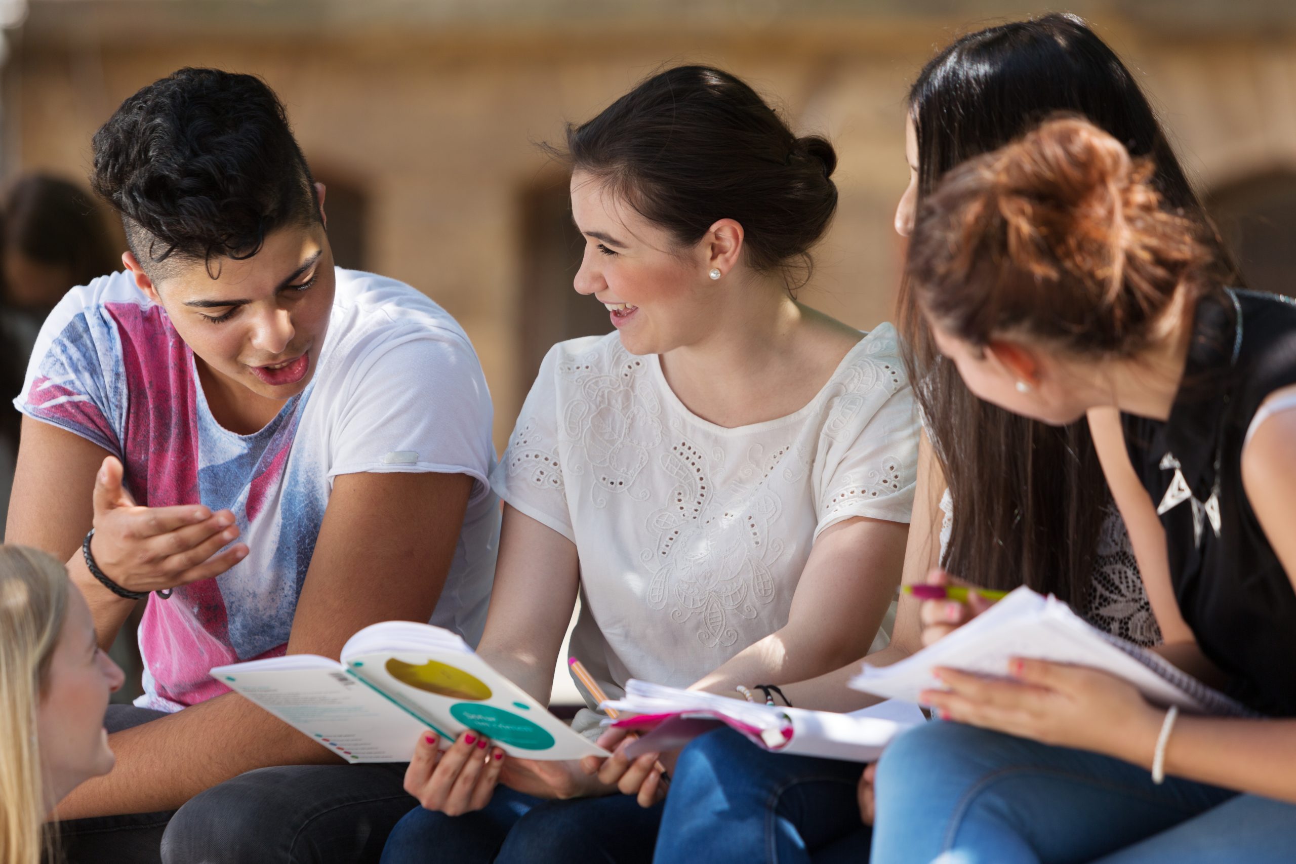 Group of students sitting outside looking at a book and talking