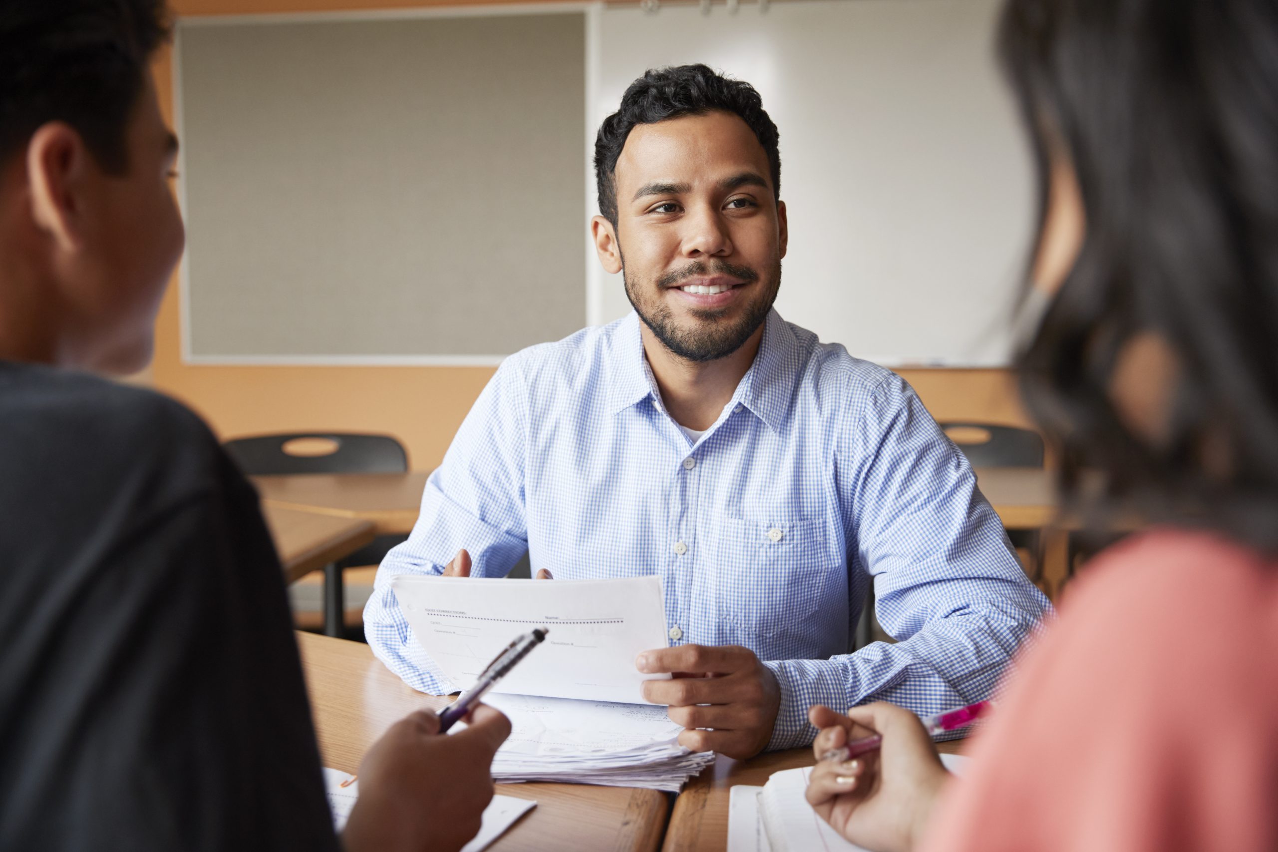 Male High School Tutor With Two Students At Desk In Seminar Notebooks and a pen