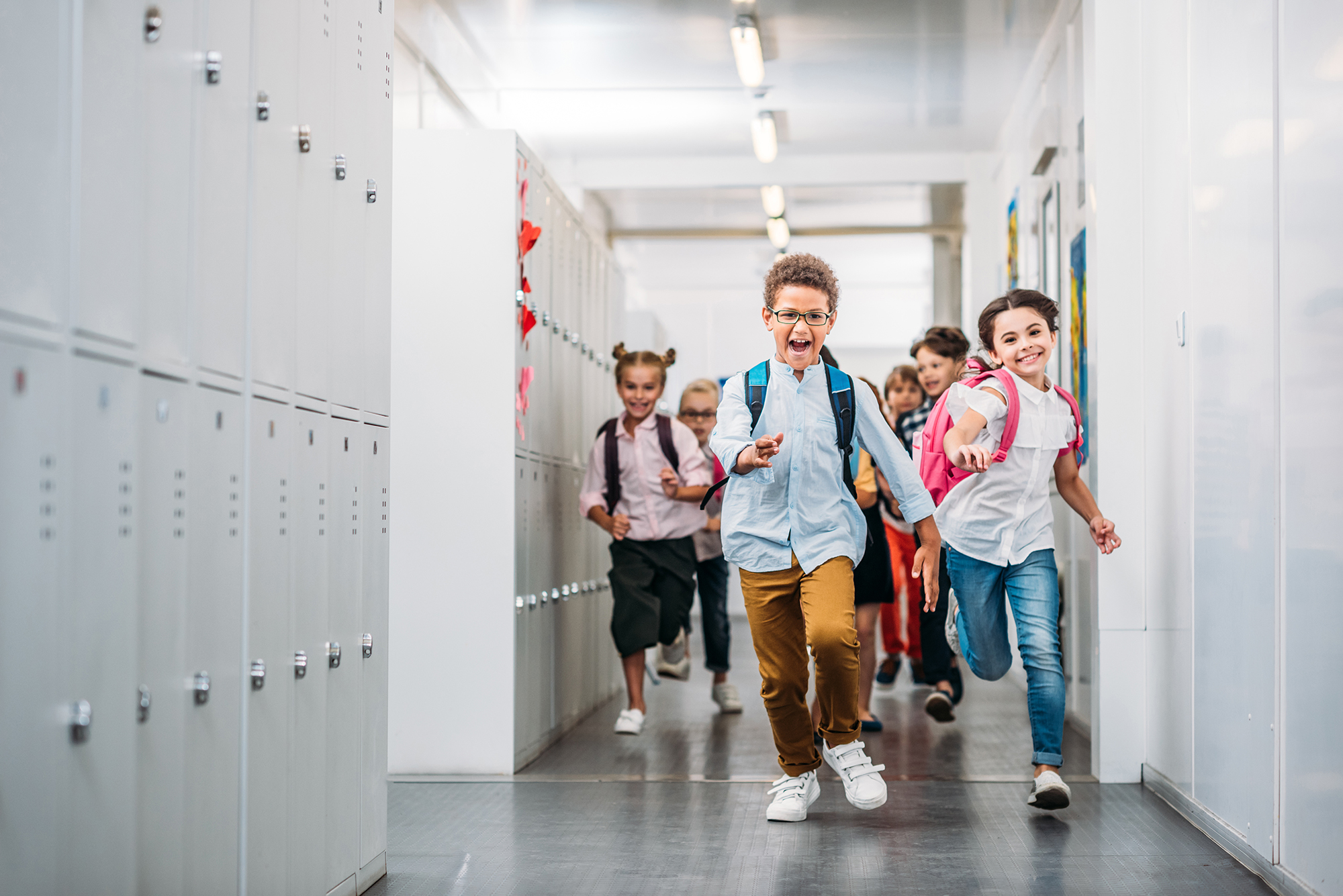 Group of students running down a school hallway, lined with lockers.