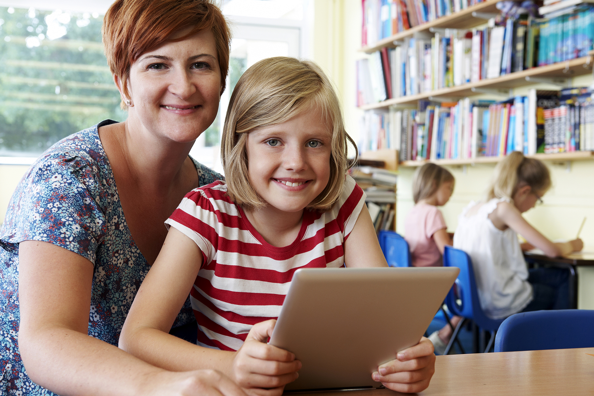 Teacher and a student sit at a table looking at a tablet.