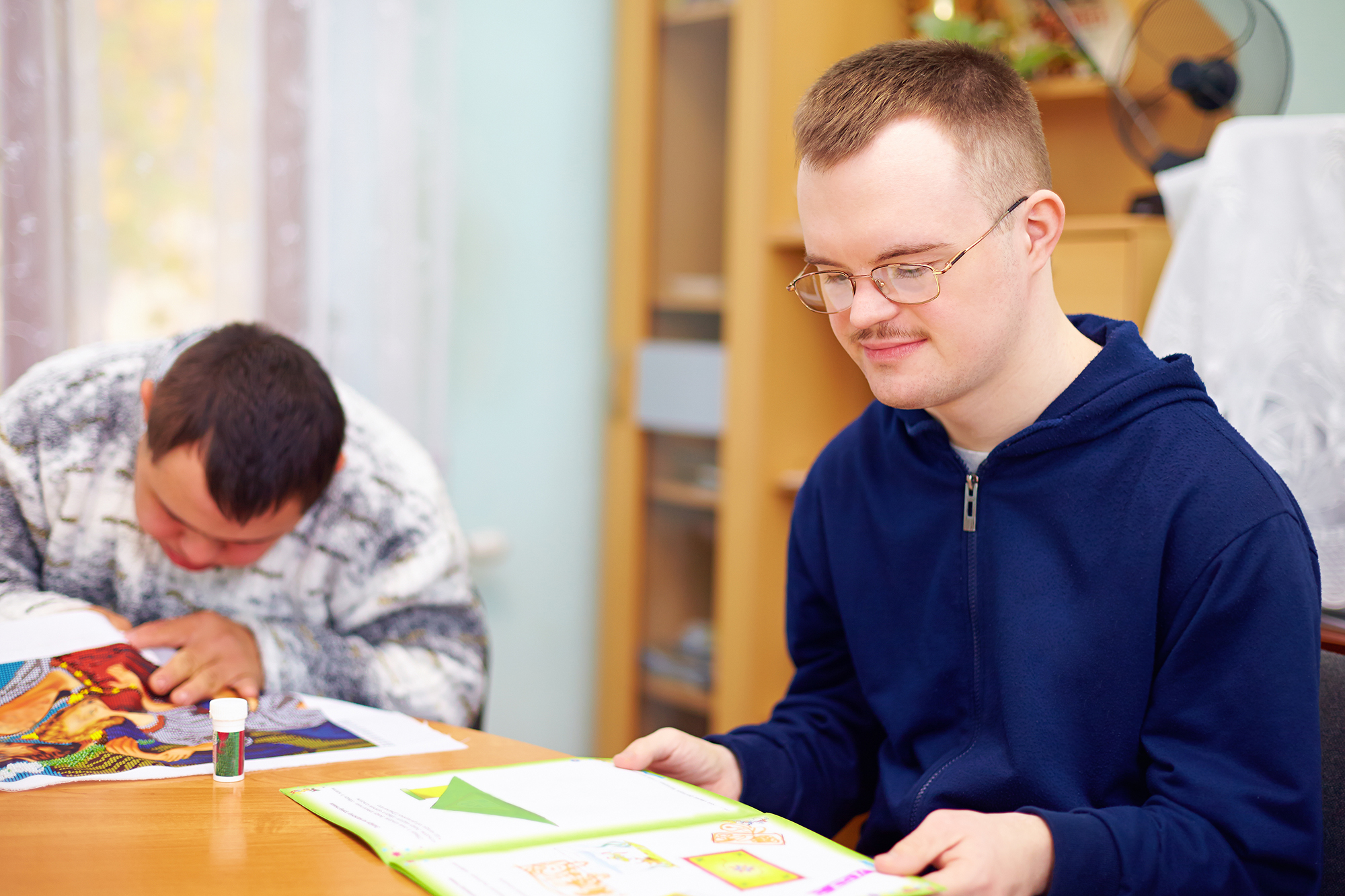 Young adult man sitting at a table reading.