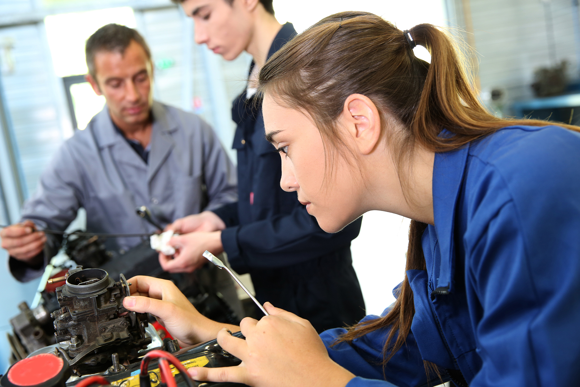 Mechanics training class with teacher and students Young woman working on a car engine in a mechanics training class.