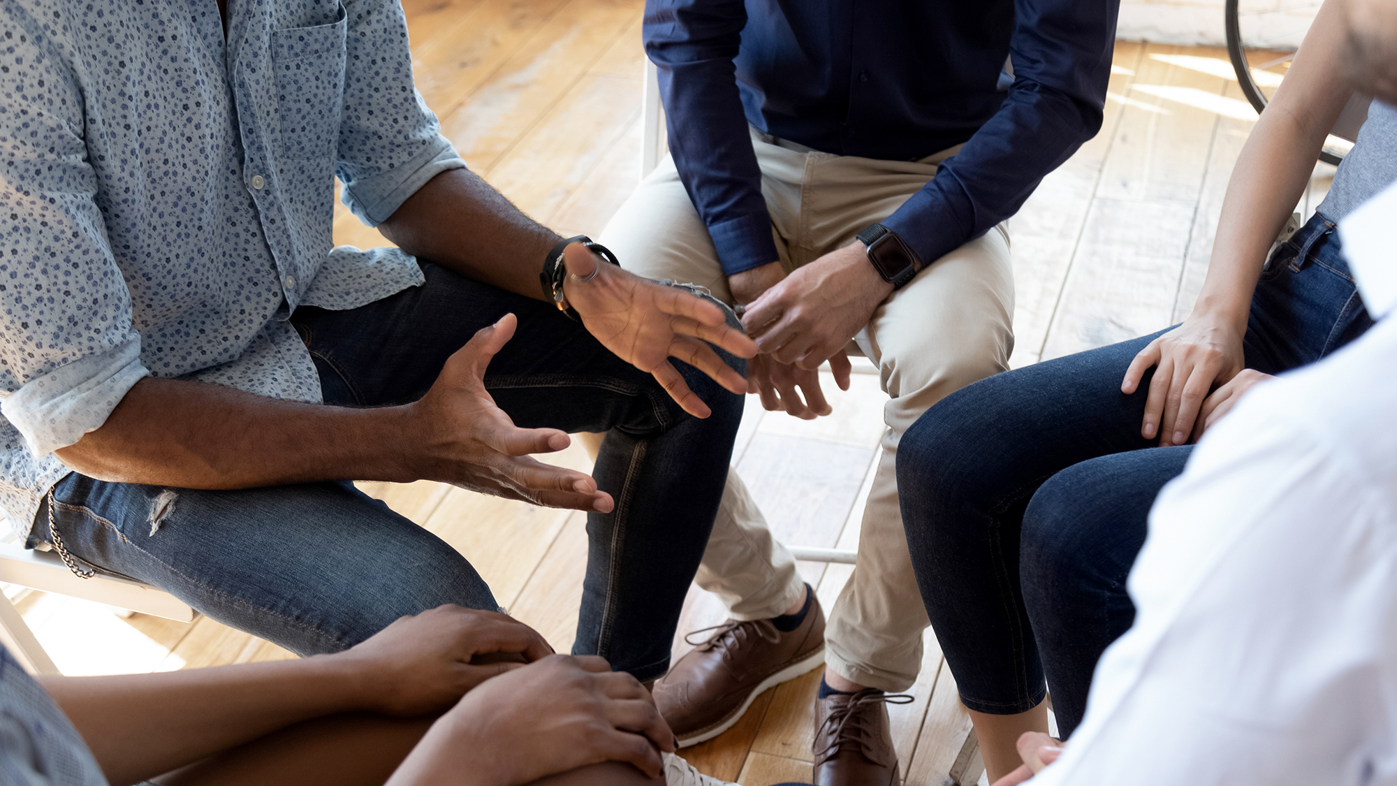 Group of people sitting in a group. Only their hands  and legs are visible. 