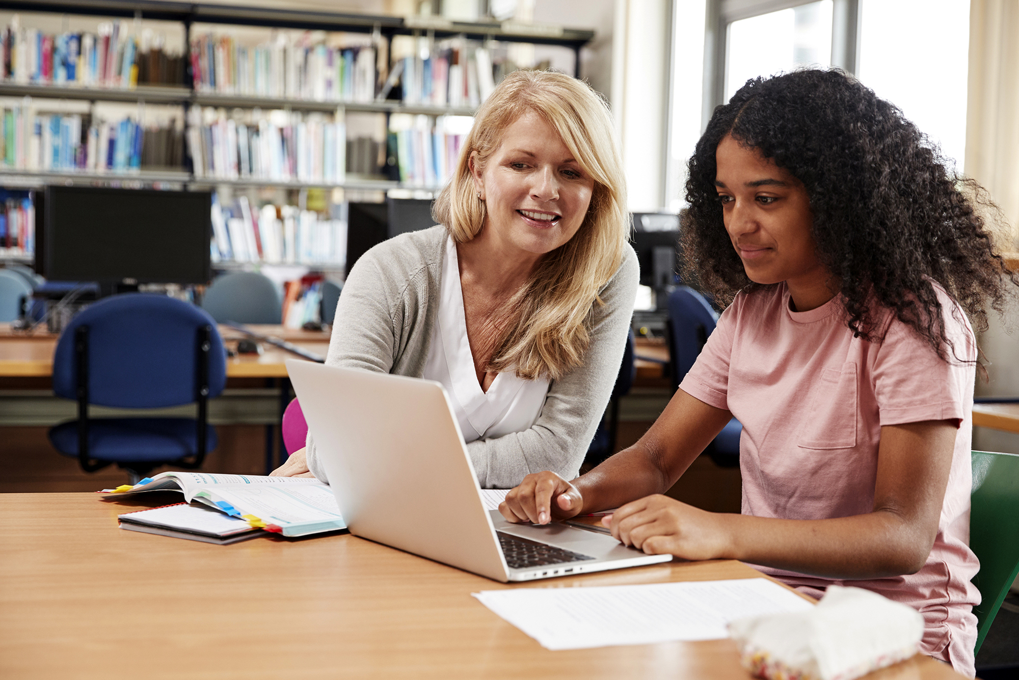 African American student and teacher sitting at a table and looking at a laptop together