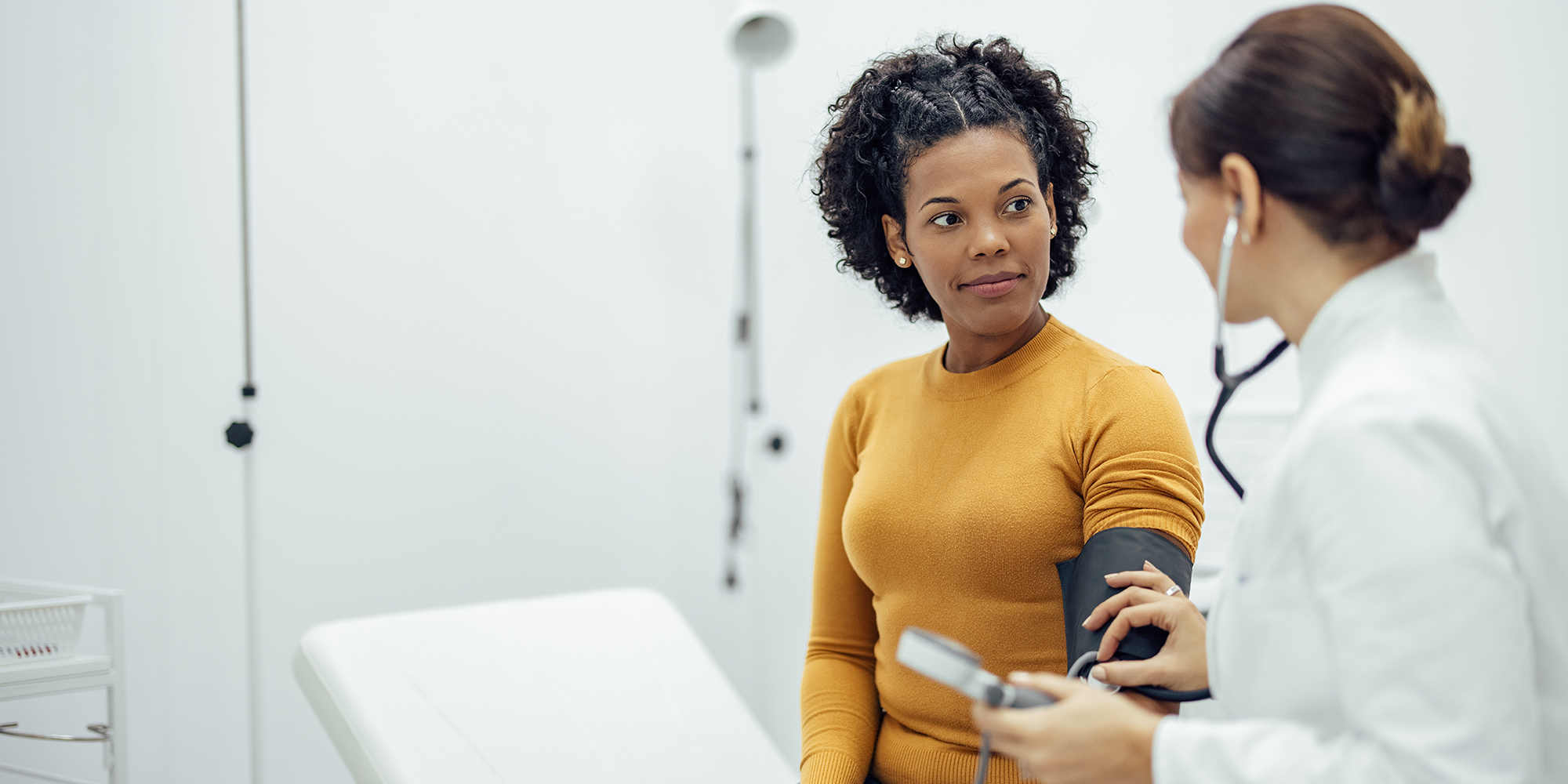 Doctor measuring blood pressure to a smiling woman as a part of a medical exam.