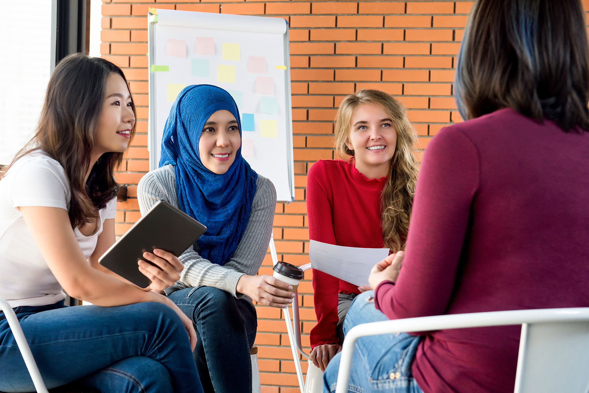 Group of diverse women in casual colorful clothes sitting in circle meeting for social project