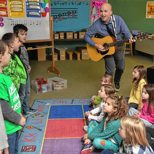 Geoffrey Gould playing guitar to school children