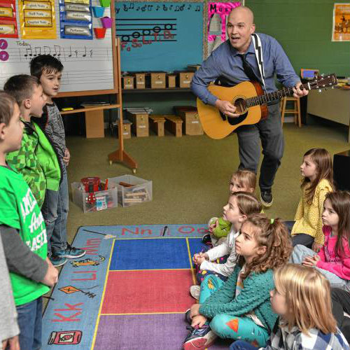 Geoffrey Gould playing guitar to school children