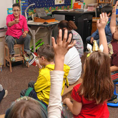 children in a classroom raising hands