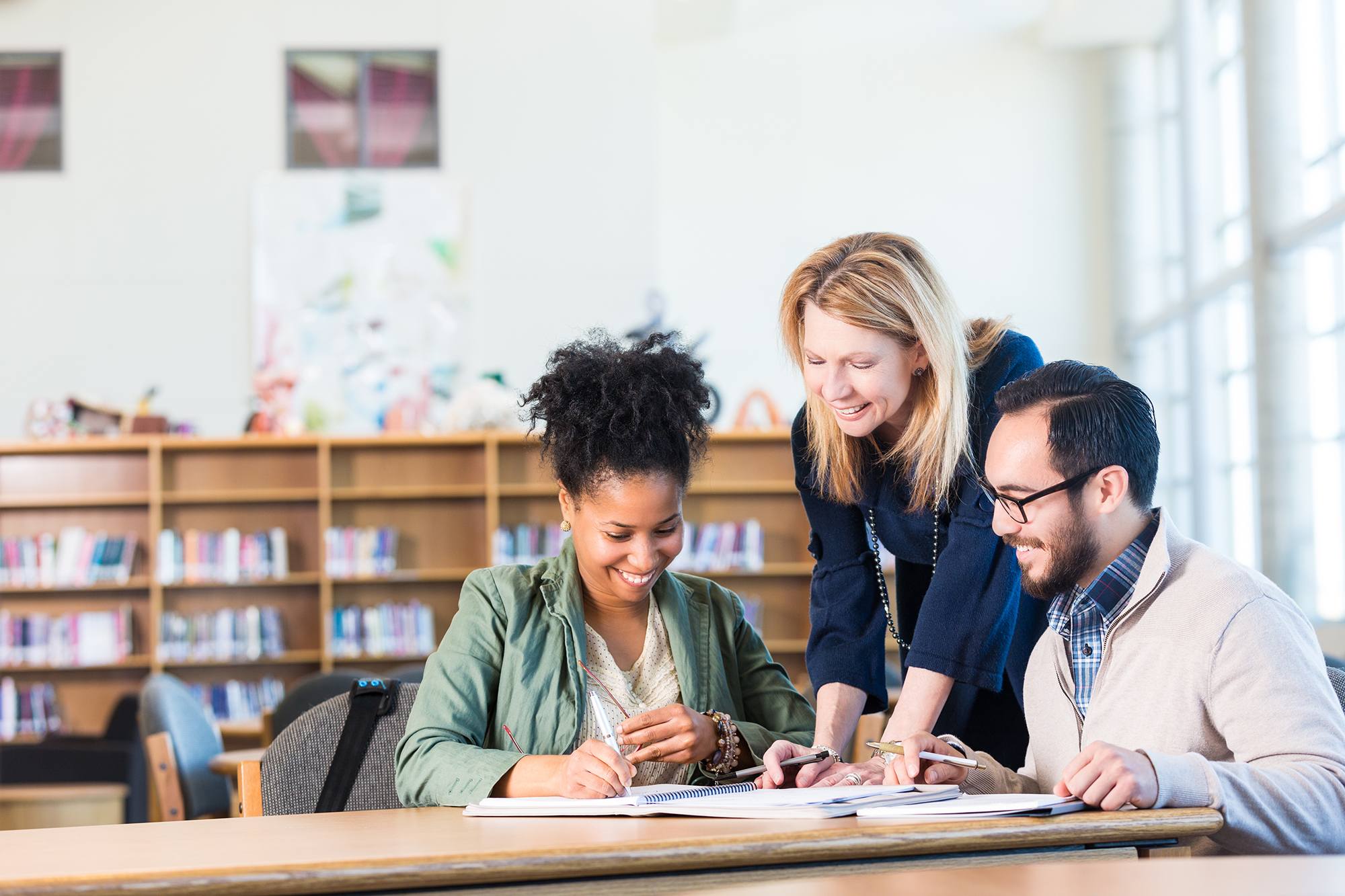 image of thre adults looking at a book together and discussing something in a library